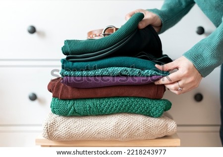 Woman's hand organizing stack of warm wool and cotton clothes. Winter autumn wardrobe concept close up