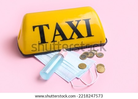 Yellow taxi roof sign, medical masks, coins and sanitizer on pink background