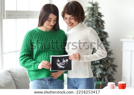 Young pregnant woman with sonogram image and her wife at home