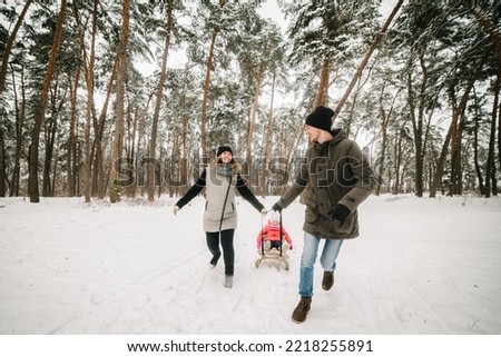 Happy family with daughter having fun in winter forest. Mom, dad, daughter running and walking in the snow in mountains. Father, mother, and child in sled walk and play in the park. Winter holidays.