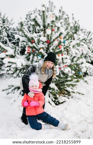 Happy family near decorated Christmas tree. Mom and girl having fun and playing on snowy winter, walking in mountain, nature. Mother and children daughter running in snow enjoying journey in forest.