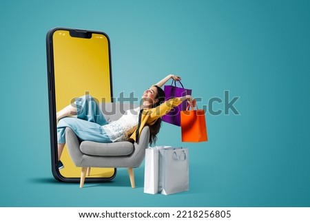 Happy fashionable young woman sitting and holding shopping bags in a smartphone, she is doing online shopping, blank copy space Royalty-Free Stock Photo #2218256805