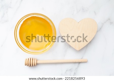 Honey in a bowl, a honey spoon and an empty wooden heart. Top view. Flat lay. Marble background