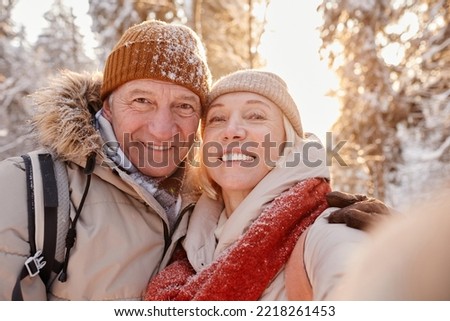 POV portrait of happy senior couple taking selfie photo while enjoying hike in winter forest