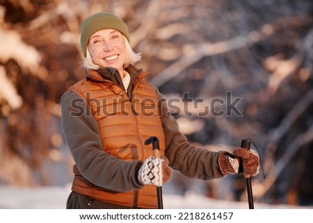 Waist up portrait of smiling mature woman enjoying Nordic walk in winter forest at sunset, copy space