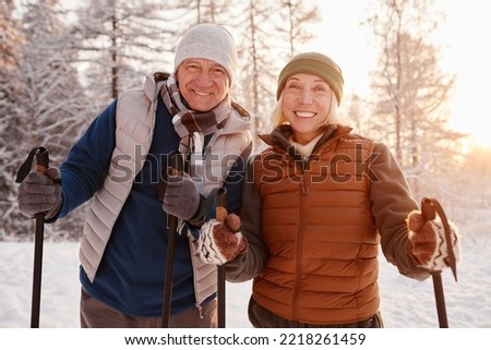 Waist up portrait of active senior couple enjoying Nordic walk with poles in winter forest and looking at camera