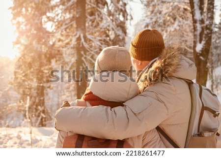 Back view of mature couple embracing in winter forest lit by sunlight, copy space