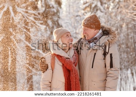 Waist up portrait of loving senior couple embracing in winter forest with snow falling