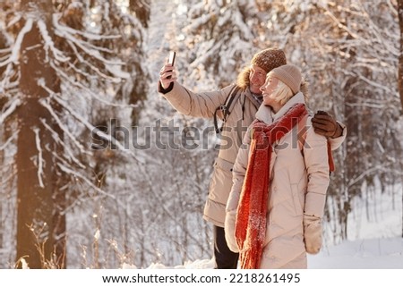 Side view portrait of active mature couple taking selfie photo while enjoying hike in winter forest, copy space