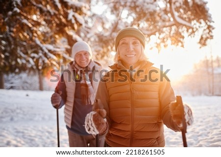 Waist up portrait of smiling mature couple enjoying Nordic walk in winter forest at sunset