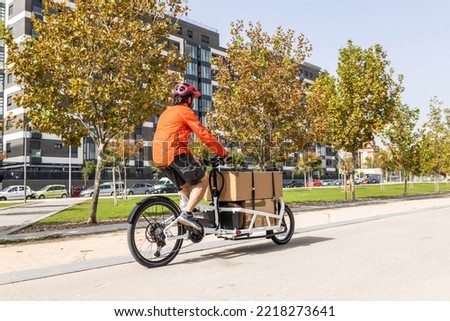 young courier with red clothing and helmet riding cargo bike , riding along the city bike path on his way to deliver a package.