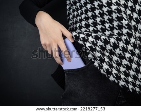Mobile phone in a pocket close-up. A woman's hand takes out a phone from her pocket. Black background. Lilac cover. Royalty-Free Stock Photo #2218277153