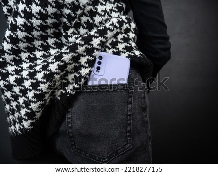 Mobile phone in a pocket close-up. A woman's hand takes out a phone from her pocket. Black background. Lilac cover. Royalty-Free Stock Photo #2218277155