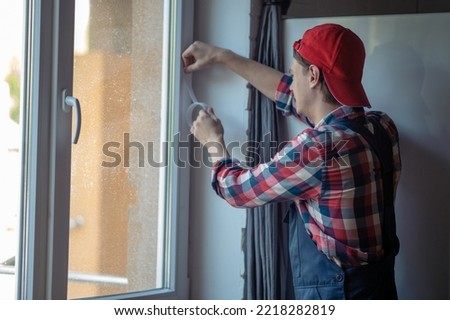 Skilled Caucasian serviceman weather-stripping the home window Royalty-Free Stock Photo #2218282819