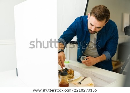 Handsome caucasian photographer doing food styling of pancakes during a photo shooting at his studio