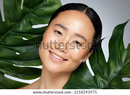 Face, beauty and asian woman with monstera leaf on gray studio background. A beautiful Japanese woman with healthy, glowing and flawless skin, skincare routine and makeup with organic plant cosmetics