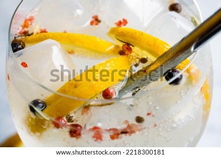 Gin with Sicilian lemon and spices containing tonic water, ice and a straw. Pink pepper, juniper, rosemary and cinnamon sticks are used. Mention of bars and get-togethers.