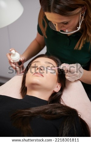 Close up of beauty specialist in sterile gloves applying cleansing mousse on woman eyelashes with cosmetic lash brush. Eyelash stylist preparing woman lashes for applying extensions. Royalty-Free Stock Photo #2218301811
