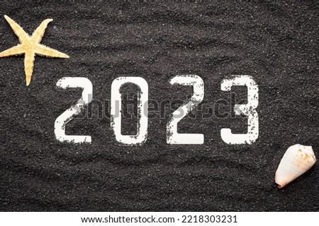 Happy New Year 2023 concept with a shell and a starfish on black beach sand. Winter vacations in the sun.	