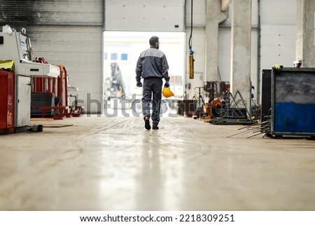A metallurgy worker leaves work and goes towards the exit of the factory. Royalty-Free Stock Photo #2218309251