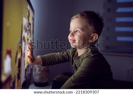 A bedtime ritual for young children. The boy touched the TV screen with one hand. A close-up portrait of a kid in pajamas sitting right in front of the TV and staring at a cartoon