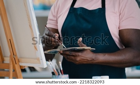 Close-up of male hands unrecognizable African man artist painter holding palette with bright oil acrylic paints colors drawing creates picture on canvas and easel using painting with brushes draw