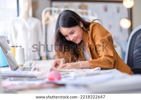 Young professional clothes fashion designer sitting near sewing machine use laptop computer and tablet pc to reference and concentrate on her work pattern