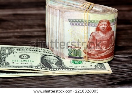 Folded Egyptian money  200 LE and pile of American money isolated on wood, two hundred Egyptian pounds  cash money bills folded up with rubber bands and one dollar bill isolated on wooden background Royalty-Free Stock Photo #2218326003