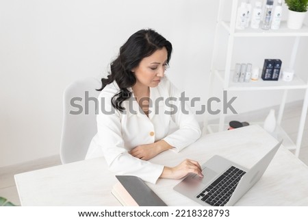 Indian woman beautician takes notes in office with laptop - cosmetologist business woman or doctor concept