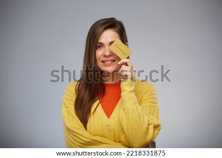 Smiling woman in yellow holding credit card in front of eye. Isolated female advertising portrait.