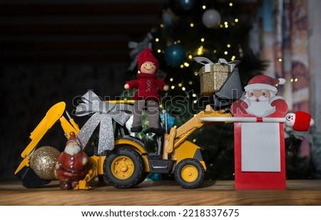 concept of new year business greetings in construction company. toy bulldozer - excavator, souvenir Santa Claus, festive notebook with place for advertising inscription on background of Christmas tree