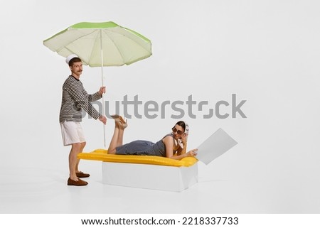 Portrait of young beautiful woman lying on inflatable mattress and sailor man holding umbrella isolated on white background. Concept of summer holidays, retro fashion, vintage style. Copy space for ad