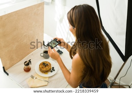 High angle of a woman influencer taking pictures of food with her smartphone for social media at a professional studio