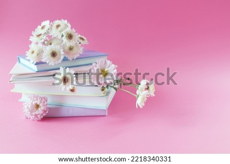 A stack of books with bookmarks from fresh chrysanthemum flowers, on a pink background, the concept of education, back to school, reading, library, congratulations, postcard
