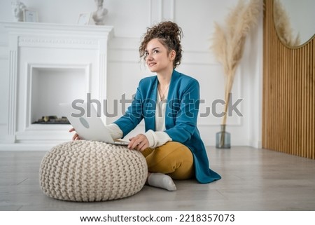 One woman young adult caucasian female sitting on the floor at home with laptop computer working and looking to the side happy smile freelance brunette with curly hair domestic life copy space
