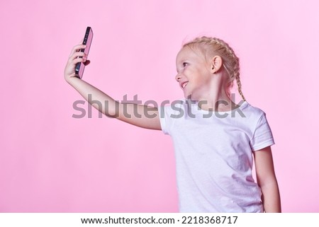 Cute little girl taking a selfie, posing in front of a phone, using a front camera