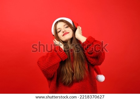 Happy woman listening to music with headphones wearing santa hat on red background. Enjoy holiday songs.