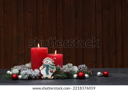 Red candles with Christmas decorations in front of a rustic wooden wall.