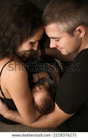 Young parents with their little baby on a dark background, from above