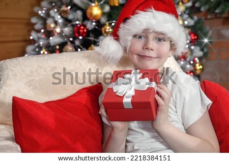 Merry Christmas kids. A boy in a Santa hat with a gift from Santa Claus, near a Christmas tree with Christmas lights and a fireplace. Family Christmas.