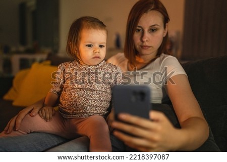 Small caucasian child little girl toddler mother and daughter sitting in dark room at night at home on sofa bed watching cartoons or movies on mobile phone real people family growing up copy space