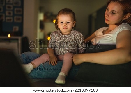 Small caucasian child little girl toddler mother and daughter sitting in dark room at night at home on sofa bed watching cartoons or movies on laptop computer real people family growing up copy space