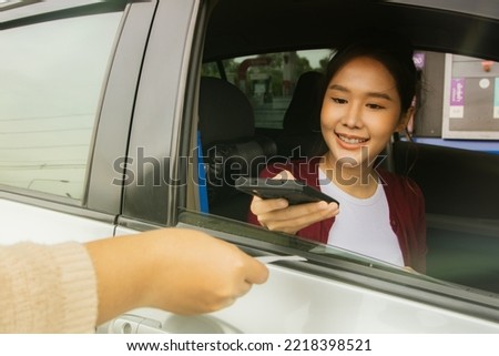 Asian woman drives a sedan, refuels at a gas station, pays for services by scanning barcodes with her smartphone, transfers money from credit cards instead of cash. Royalty-Free Stock Photo #2218398521