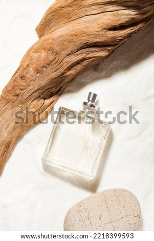 Perfumery. Sea ​​breeze idea. Transparent perfume bottle on a sand near the weathered wooden snag and stone. Top view. Vertical composition. Royalty-Free Stock Photo #2218399593