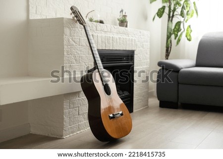 Minimalistic interior design concept. Acoustic guitar on grey textile sofa in spacious room of loft style apartment with wood textured laminated flooring. Background, copy space, close up