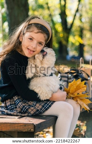 Little girl with dog in forest. Child girl with autumn leaf. Fall background. Portrait beautiful autumn girl kissing dog in fall forest background. Best friends
