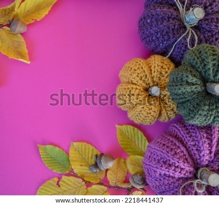 colorful autumn leaves with handmade crochet pumpkins on pink ground with space for text fall background
