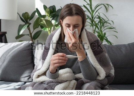 Seasonal contagious grippe illness concept. Ill woman covered plaid feel sick unwell. Unhealthy female measuring body temperature with electronic thermometer, suffer from flu sitting on sofa at home Royalty-Free Stock Photo #2218448123