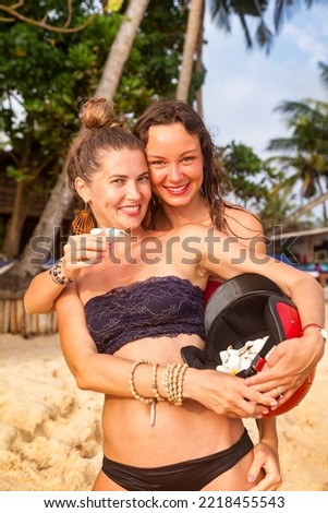 Lesbian couple women hugging on sandy beach at tropical palm trees background. Lifestyle portrait two happy lgbtq females resting in tropic. Summertime vacation tourism concept. Copy text space