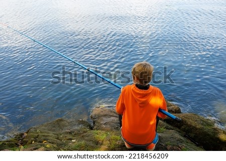 the boy sits with his back and catches fish with a fishing rod in the river